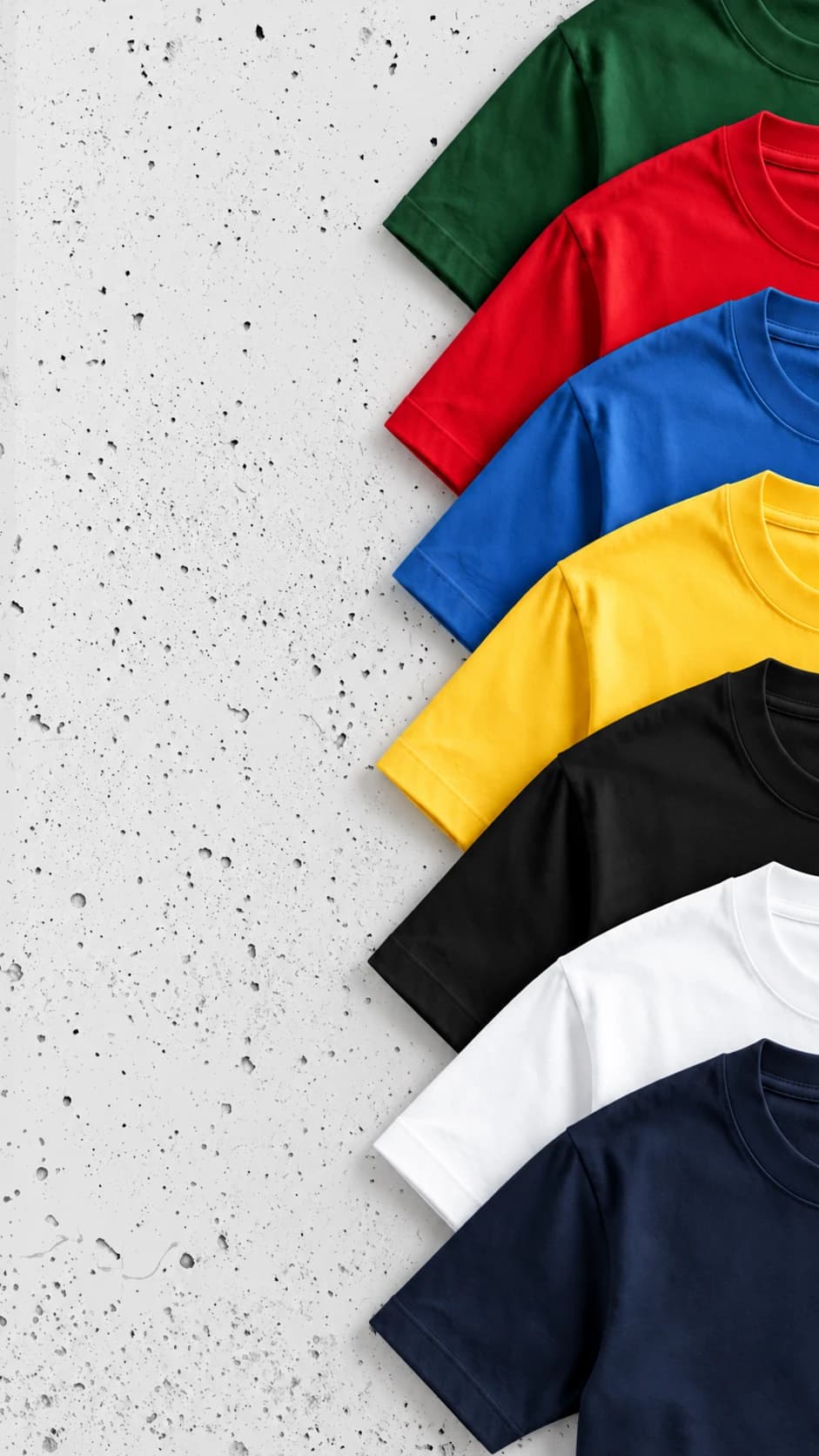 Seven blank tees fanned out on concrete in green, red, royal blue, yellow, black, white and navy