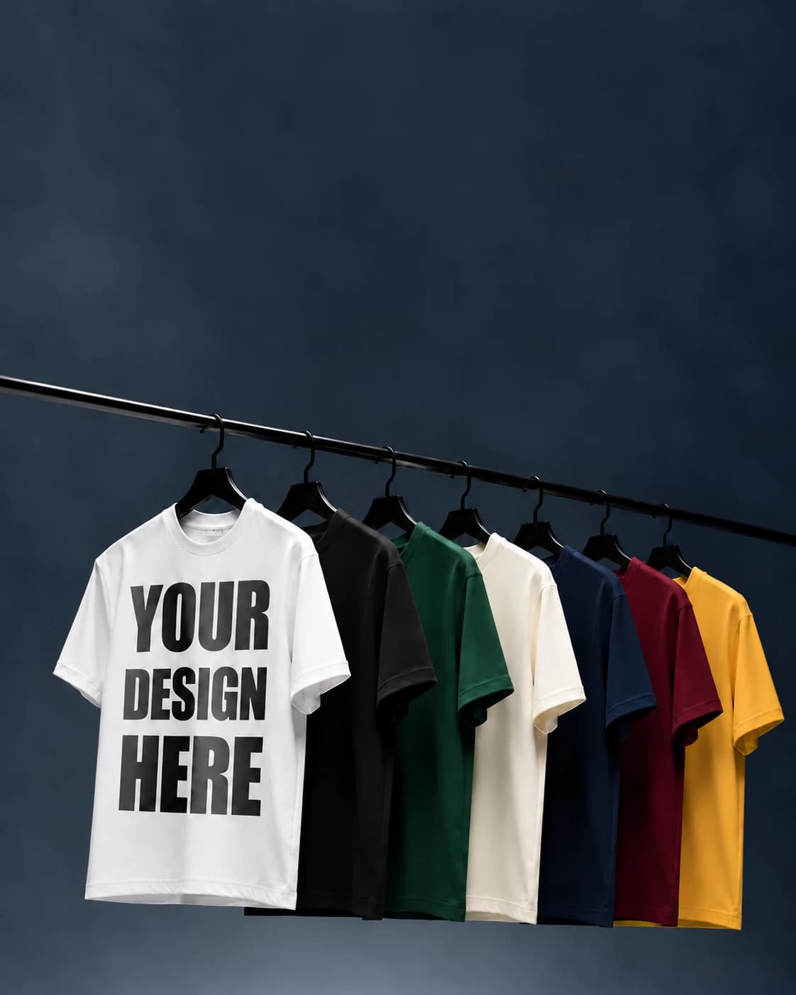 Seven heavyweight tees on a rail in white, black, green, cream, navy, maroon and gold, the white one printed with a sample design