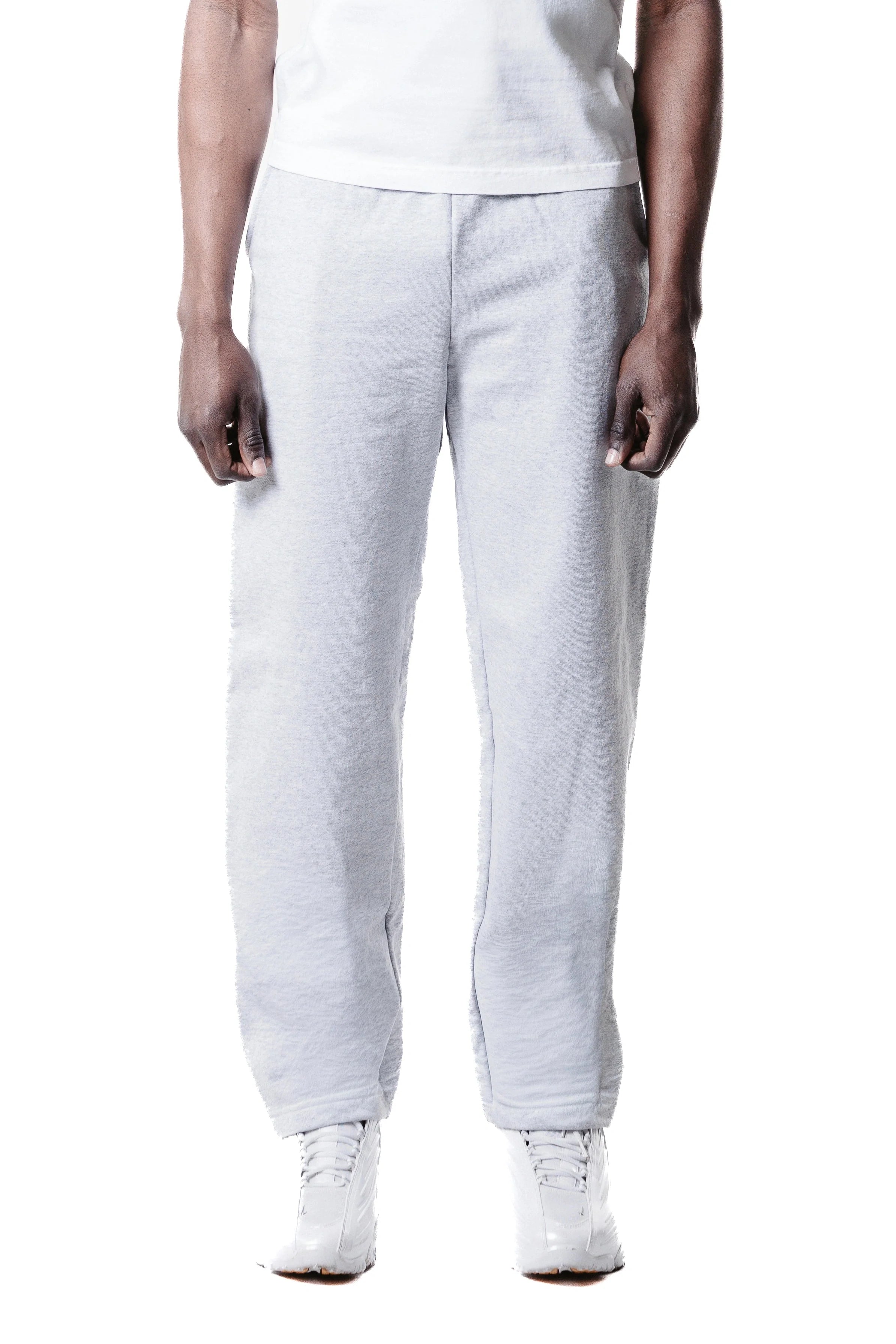 A person models wide leg baggy sweatpants in light gray with a white shirt and white shoes against a white background. The image is cropped at the shoulders, so the person's face is not visible.