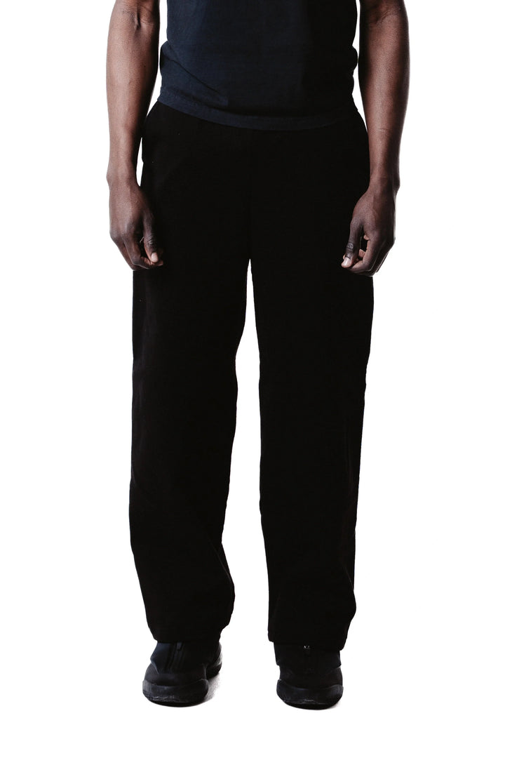 A person stands against a white background, wearing Wide Leg Baggy Sweatpants in black, along with a black shirt and black shoes. Only the lower half of the body and arms are visible.