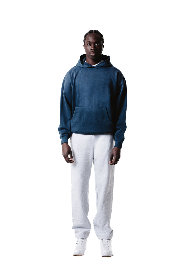 A man stands facing forward against a plain white background, wearing the Vintage Distressed Special Hoodie in dark blue, paired with light gray sweatpants and white sneakers.
